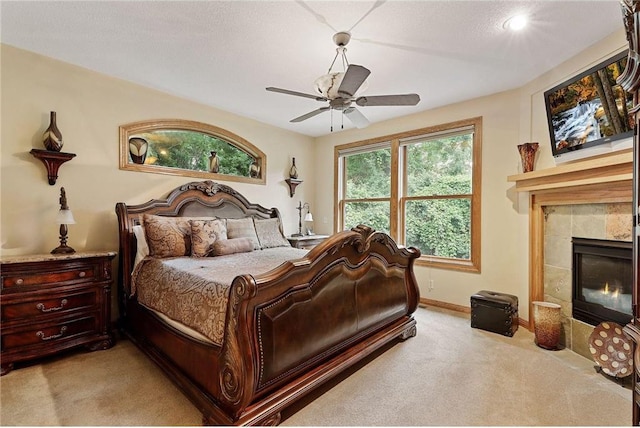 bedroom with ceiling fan, a tile fireplace, a textured ceiling, and light colored carpet