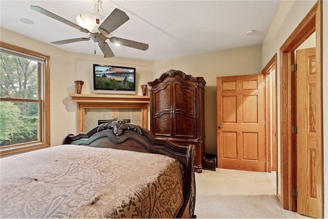 carpeted bedroom featuring a tiled fireplace and ceiling fan