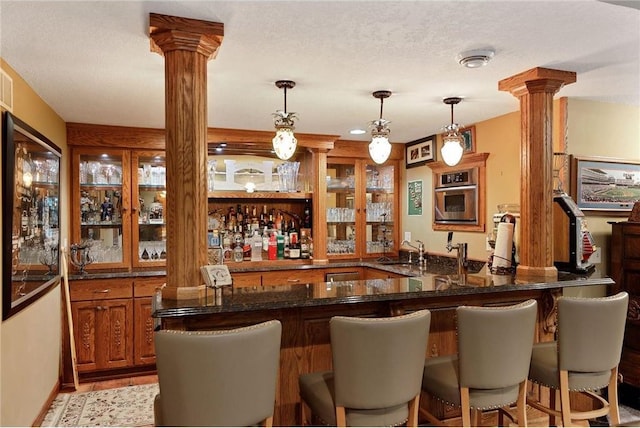 bar with decorative light fixtures, decorative columns, sink, dark stone countertops, and a textured ceiling