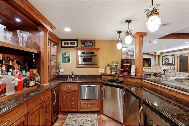 interior space with ornate columns, stainless steel oven, dark stone countertops, a textured ceiling, and hanging light fixtures