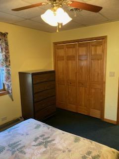 unfurnished bedroom featuring ceiling fan, a paneled ceiling, dark colored carpet, and a closet