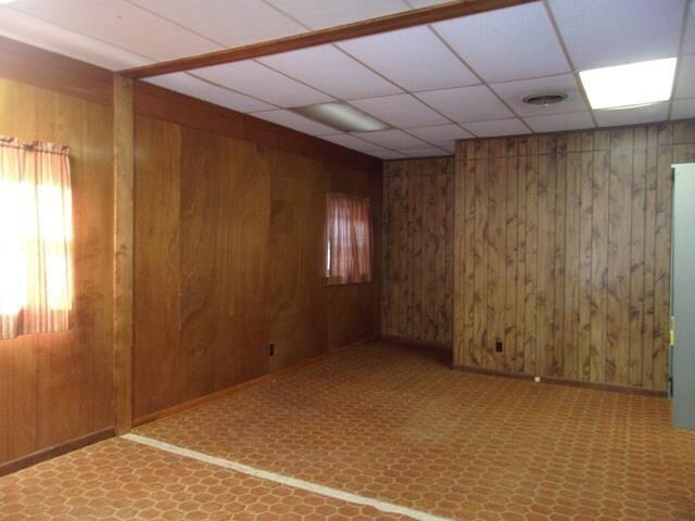 tiled spare room featuring wooden walls and a drop ceiling