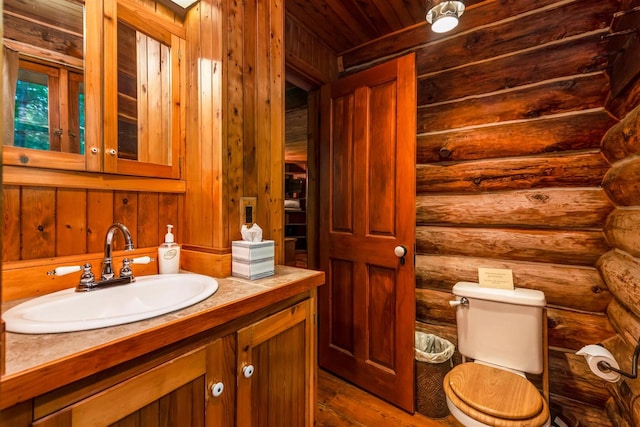 bathroom featuring hardwood / wood-style floors, vanity with extensive cabinet space, log walls, and toilet