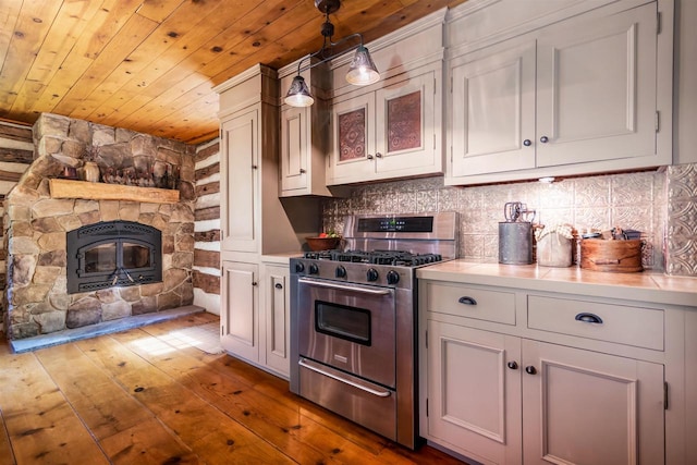 kitchen with white cabinets, stainless steel range with gas cooktop, hardwood / wood-style floors, pendant lighting, and a fireplace