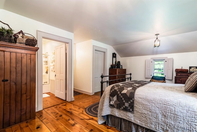 bedroom featuring lofted ceiling, ensuite bath, and light hardwood / wood-style floors