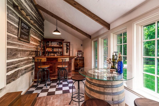 bar with wood walls, hanging light fixtures, dark tile floors, and lofted ceiling with beams