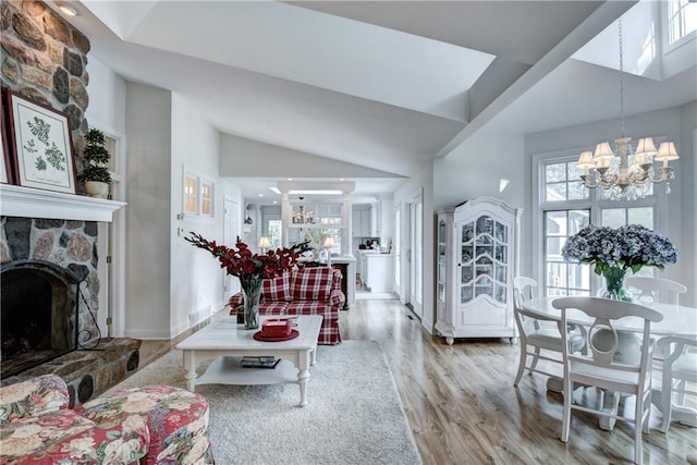 living room with a chandelier, light hardwood / wood-style floors, a stone fireplace, and high vaulted ceiling