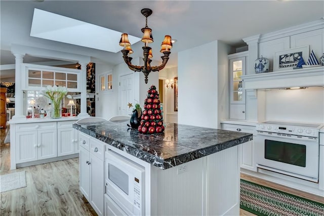 kitchen with a kitchen island, white microwave, white cabinets, range, and an inviting chandelier