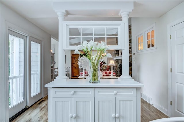 kitchen featuring plenty of natural light, ornate columns, white cabinetry, and light wood-type flooring