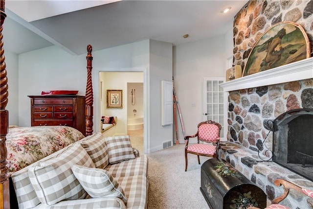 bedroom with connected bathroom, light colored carpet, and a stone fireplace