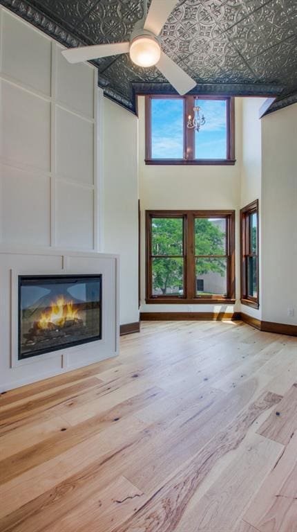 unfurnished living room with a high ceiling, ceiling fan, and light hardwood / wood-style flooring