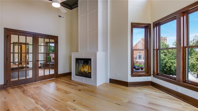 unfurnished living room featuring a towering ceiling, ceiling fan, light wood-type flooring, and french doors