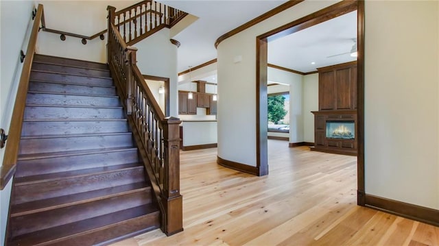 stairway featuring ceiling fan, crown molding, and light hardwood / wood-style floors