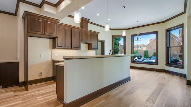 kitchen with an island with sink, hanging light fixtures, a healthy amount of sunlight, and light hardwood / wood-style flooring