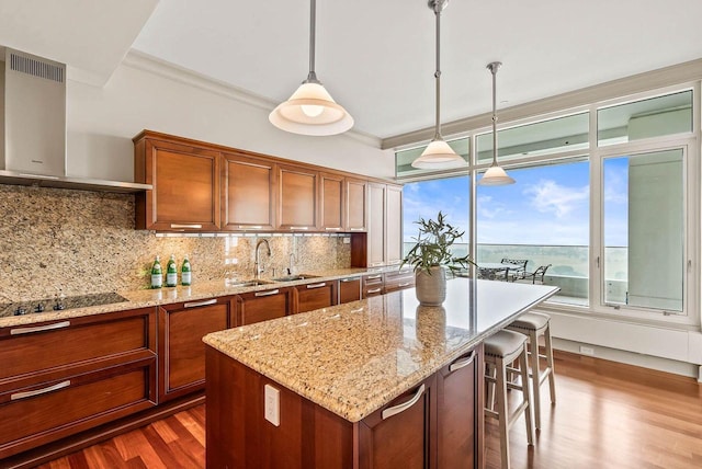 kitchen featuring sink, a kitchen island, hanging light fixtures, dark wood-type flooring, and wall chimney range hood