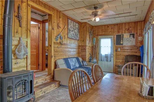 interior space with wood walls, ceiling fan, and a wood stove