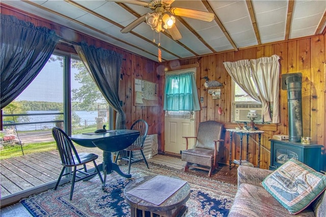 interior space with wooden walls, ceiling fan, a wood stove, and a water view