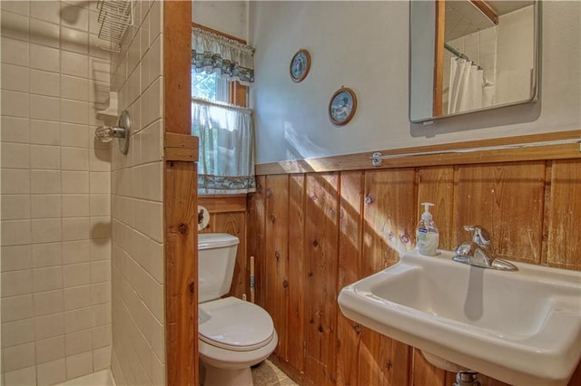 bathroom with curtained shower, sink, toilet, and wood walls