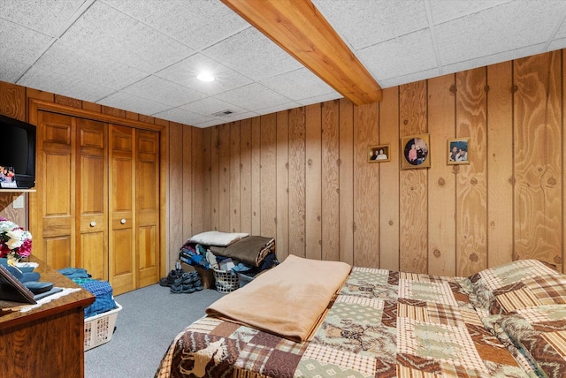 carpeted bedroom featuring a drop ceiling, wooden walls, and a closet