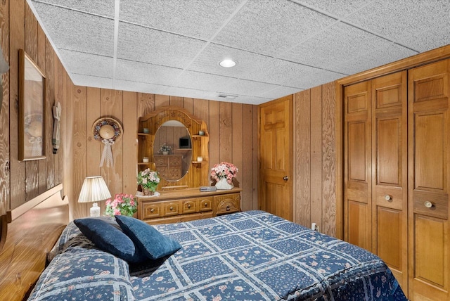 bedroom featuring wooden walls, a closet, and a paneled ceiling