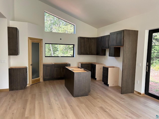 kitchen featuring high vaulted ceiling, a kitchen island, light wood-type flooring, and dark brown cabinets