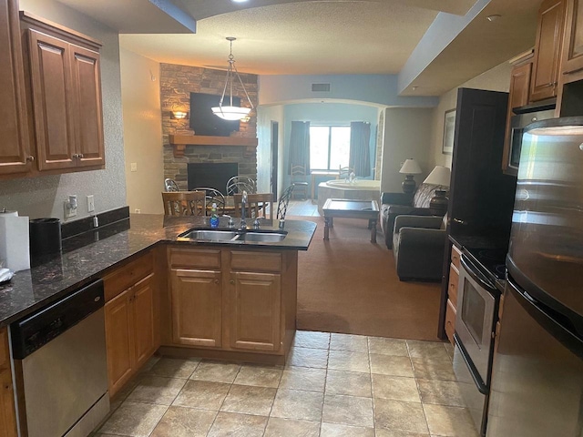 kitchen with a fireplace, kitchen peninsula, appliances with stainless steel finishes, light carpet, and sink