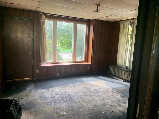 empty room featuring a wealth of natural light, a paneled ceiling, and wood walls