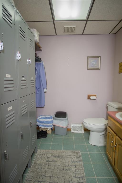 bathroom with a paneled ceiling, toilet, tile flooring, and vanity