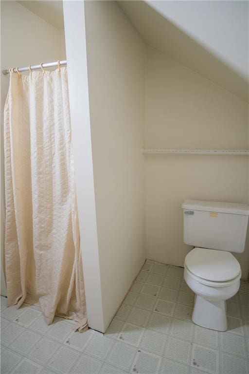 bathroom with tile floors, vaulted ceiling, and toilet