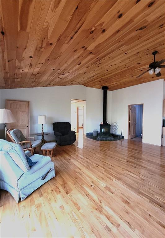 living room featuring lofted ceiling, a wood stove, wood ceiling, and light hardwood / wood-style flooring