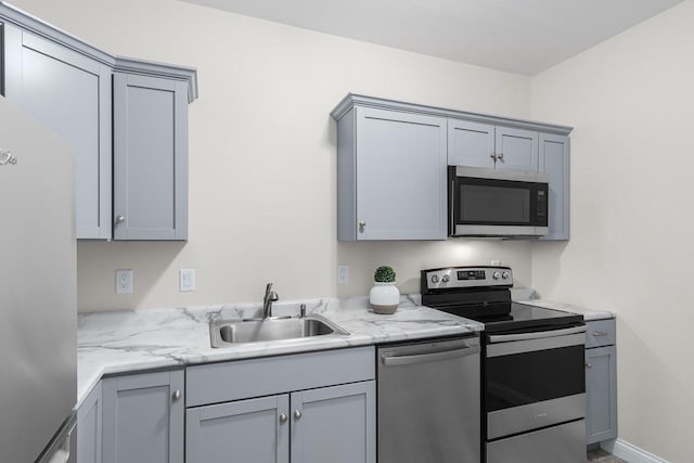 kitchen featuring appliances with stainless steel finishes, light stone countertops, gray cabinets, and sink