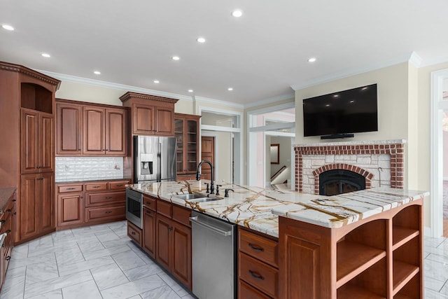 kitchen featuring an island with sink, sink, appliances with stainless steel finishes, a fireplace, and tasteful backsplash