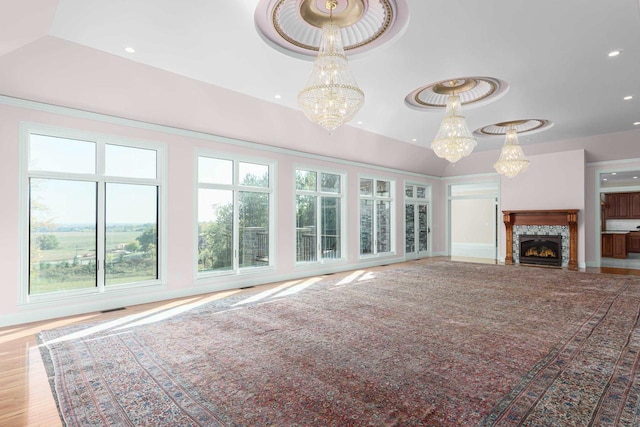 unfurnished living room featuring plenty of natural light, an inviting chandelier, light hardwood / wood-style floors, and a raised ceiling