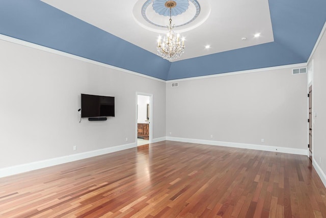 empty room featuring a raised ceiling, a high ceiling, a notable chandelier, and wood-type flooring