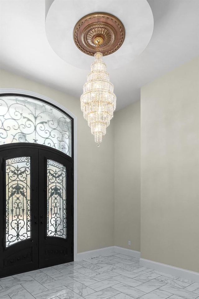 entrance foyer featuring a tray ceiling, french doors, light tile flooring, and a chandelier