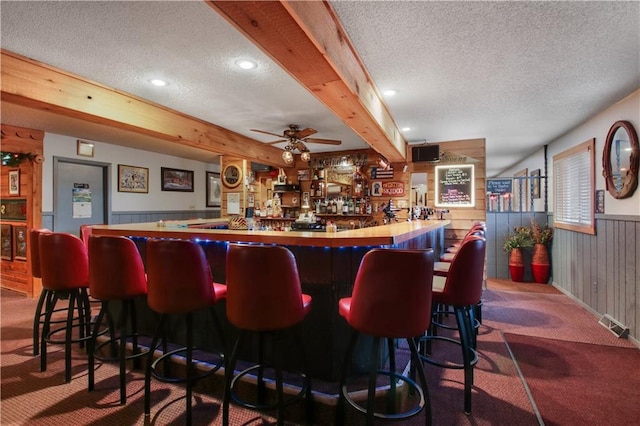 bar with carpet floors, ceiling fan, a textured ceiling, and beam ceiling