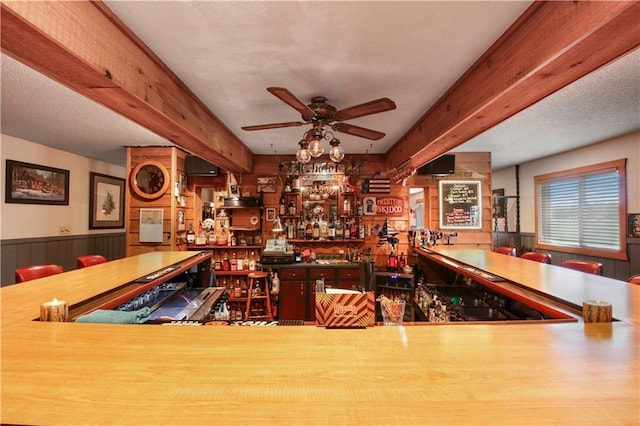 interior space with ceiling fan, indoor bar, beamed ceiling, and a textured ceiling