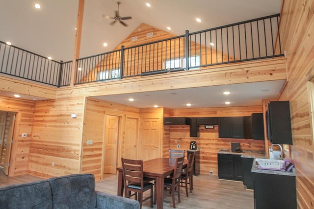 dining space with ceiling fan, light hardwood / wood-style floors, sink, a towering ceiling, and wooden walls