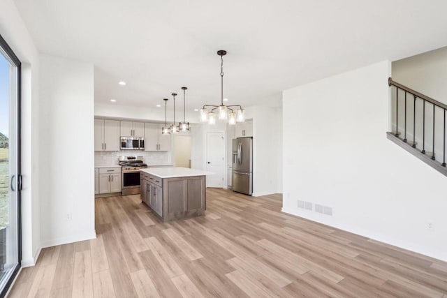 kitchen with visible vents, light wood finished floors, appliances with stainless steel finishes, a notable chandelier, and tasteful backsplash