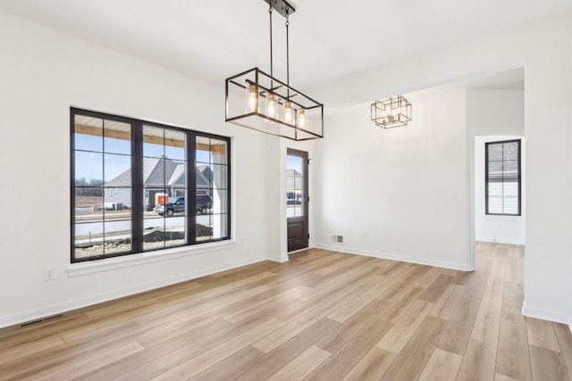 unfurnished dining area with an inviting chandelier, light wood-style floors, visible vents, and a wealth of natural light