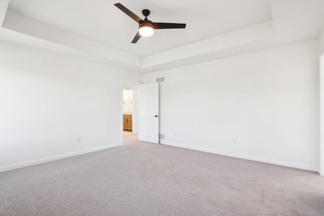 spare room featuring a tray ceiling, baseboards, light colored carpet, and ceiling fan