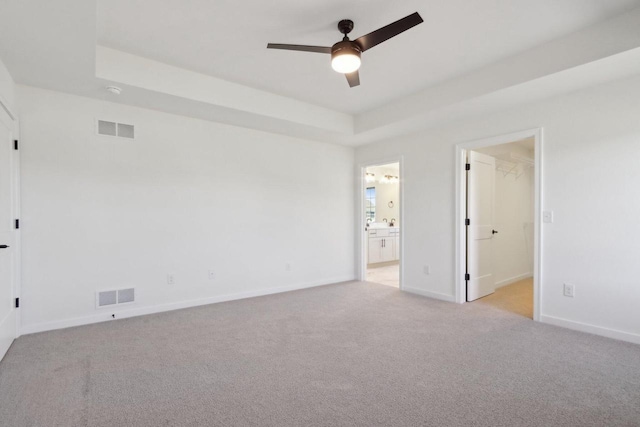 unfurnished bedroom with visible vents, a raised ceiling, light colored carpet, and baseboards