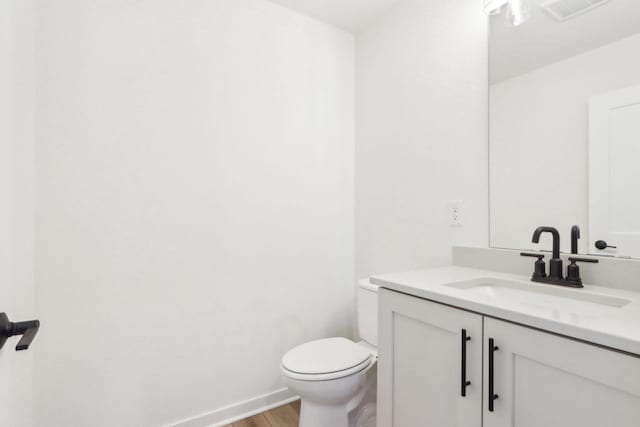 half bathroom featuring vanity, wood finished floors, visible vents, baseboards, and toilet