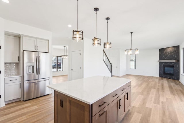 kitchen featuring light wood finished floors, a kitchen island, open floor plan, a fireplace, and stainless steel fridge