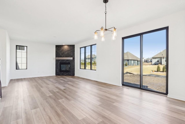 unfurnished living room featuring a chandelier, baseboards, a high end fireplace, and wood finished floors