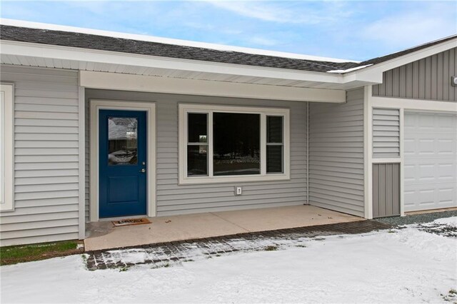 snow covered property entrance with a garage and covered porch