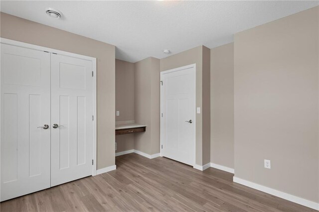 unfurnished bedroom with a closet, built in desk, and light wood-type flooring