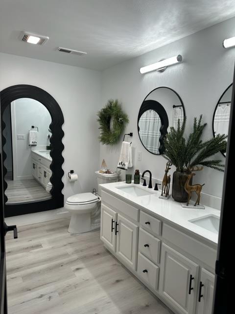 bathroom featuring toilet, dual vanity, and hardwood / wood-style flooring