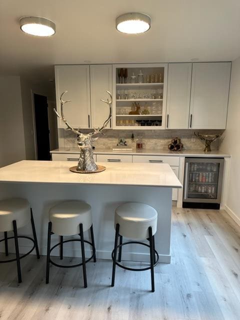 kitchen featuring white cabinets, beverage cooler, a breakfast bar area, and light wood-type flooring