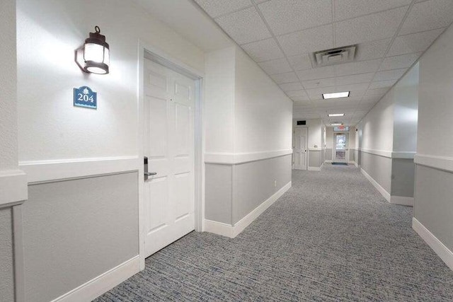 corridor featuring carpet flooring and a paneled ceiling